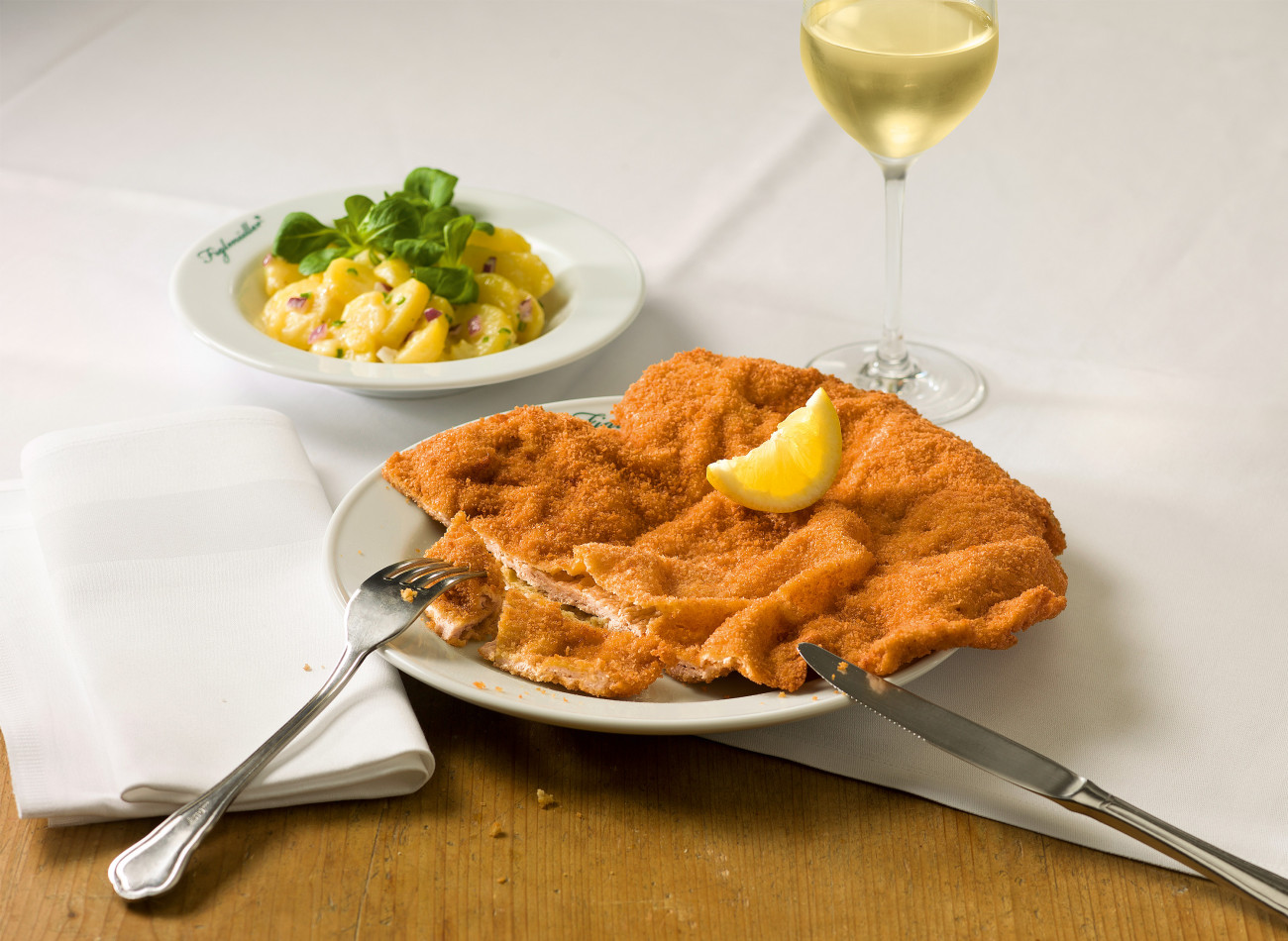 Original Figlmüller Wiener Schnitzel mit Zitrone, Kartoffelsalat und einem Glas Wein.