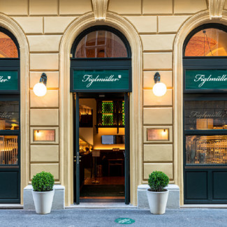 Straßenansicht des Eingangs vom Restaurant Figlmüller in der Bäckerstraße mit cremefarbener Fassade, Rundbögen und grüner Beschriftung.