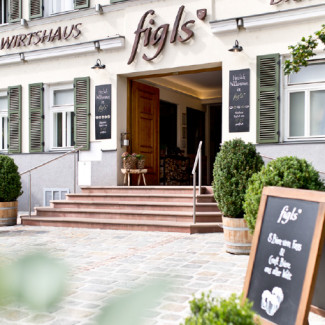Straßenansicht des Wirtshauses Figls mit Eingang, Stufen und Kreidetafel.