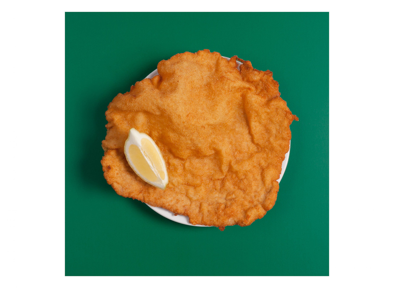 Das originale Figlmüller Wiener Schnitzel - serviert mit Zitrone auf grünem Hintergrund.