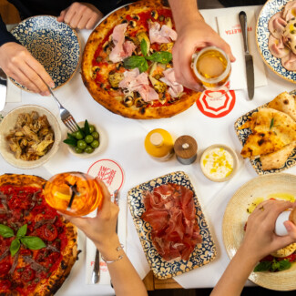 Figoletta Wien – italienische Pizza, Antipasti und Prosciutto auf dem Tisch, dazu Aperitif-Drinks.